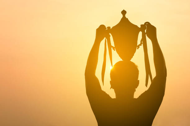 istock silhouette of a man holding up trophy on sunset sky 920219292