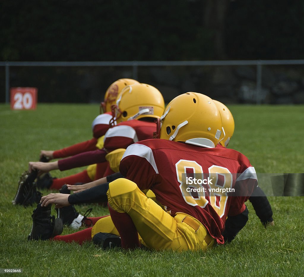 Young football athletes in uniform stretching on grass Group of pee-wee football players stretching out before the big game. Taken with a Nikon D200, ISO 200, F/5.6, 135mm, 1/320 sec. American Football - Ball Stock Photo