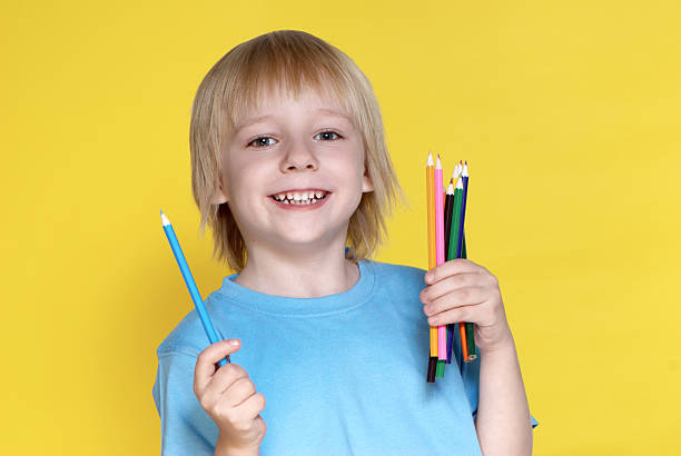 The small schoolboy with pencils on a yellow background stock photo