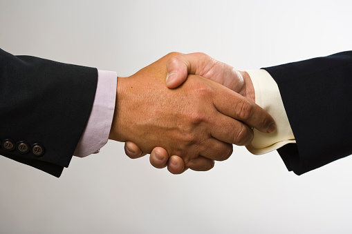 Two businessmen shake hands on the background of office building windows, partnership concept, close up