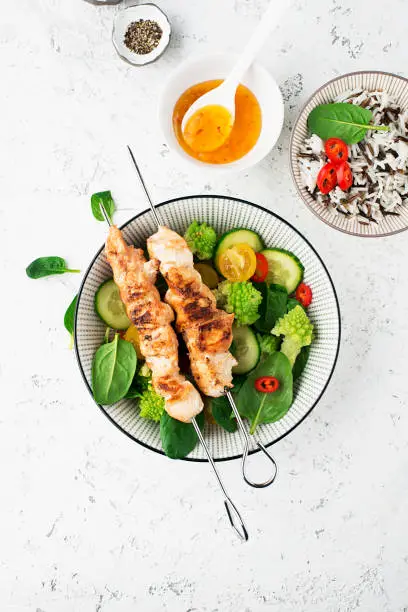 Photo of Chicken turkey skewers with fresh vegetables: spinach, hot pepper, romanesque, broccoflower, cherry tomatoes. Top view. Food concept
