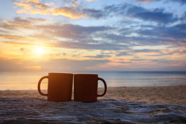 istock Coffee cup on wood log at sunset or sunrise beach 920273368