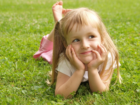 A small beautiful blonde girl in a blue linen sundress against a background of tall grass