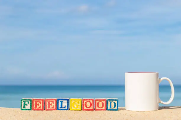 word FEELGOOD in colorful alphabet blocks and coffee cup on tropical beach, Phuket Thailand