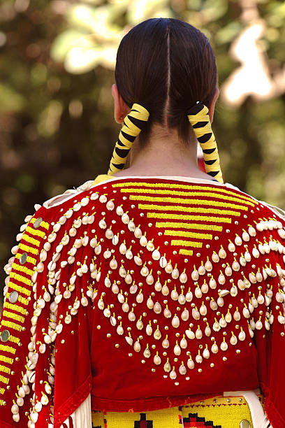 Indian maiden in traditional red costume A young American Indian girl in colorful traditional costume with braided hair at a pow wow in Hawaii.  Ribbons and shells adorn her braided hair and patterned clothing. A vertical close-up color photograph of the back of a young girl, selective focus, narrow depth of field, with red, yellow, white and green colors, shot outdoors under natural light conditions. hopi culture photos stock pictures, royalty-free photos & images