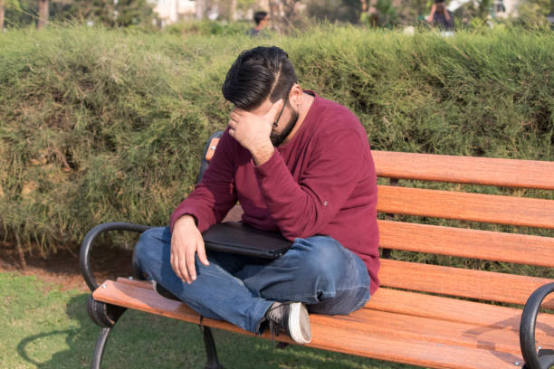 Stressed young man sitting on park bench with laptop
