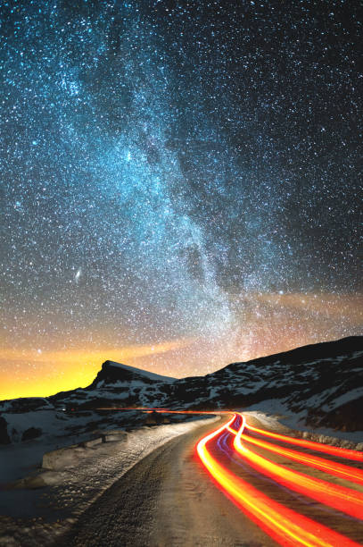 paysage de nuit. ciel de nuit avec un hémisphère nord voie lactée et des étoiles. la route de nuit éclairée par la voiture enroule avec une serpentine et laisse à une distance d’un pied d’un rocher aigu. sentiers de lumière de couleur rouge. le concept du chemin vers la connaissance et - long exposure rock cloud sky photos et images de collection