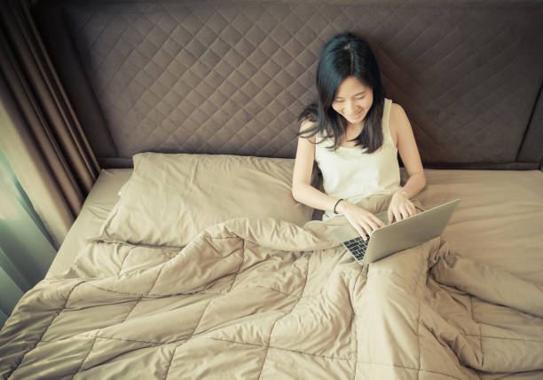 istock Happy Asian woman using a laptop on bed in bedroom 920342638