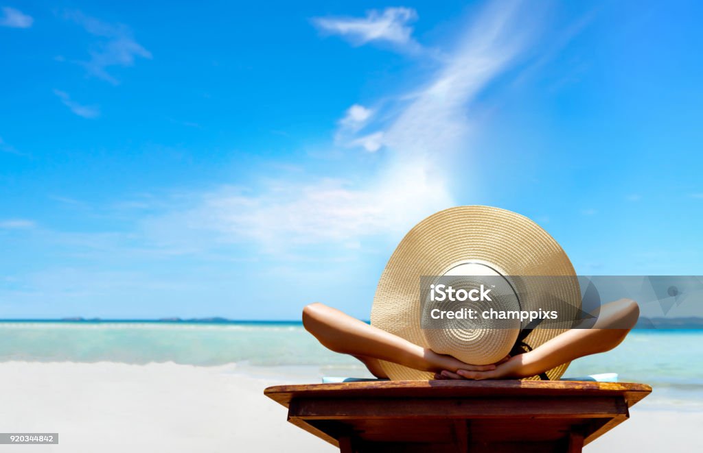 Bikini woman sexy in relax beach and resting resort in vacation on summer season with sunhat sitting chair sunbath with swimsuit alone at island lifestyle on weekend holidays Beach Stock Photo