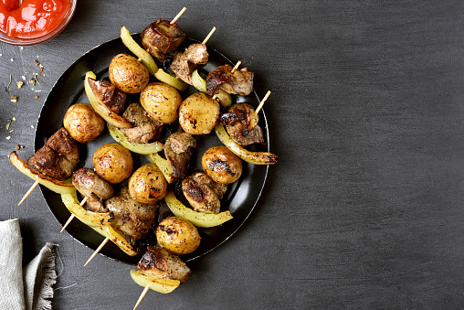 Chicken liver, potato and bell pepper on skewers over black background with copy space. Top view, flat lay