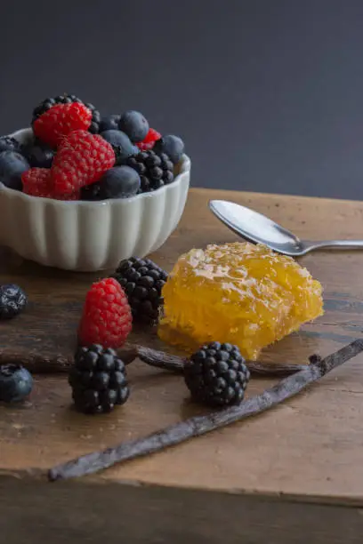 Blackberries, Raspberries, Bilberries in a white bowl, Vanilla Bean and Honeycomb with a spoon on a wooden surface