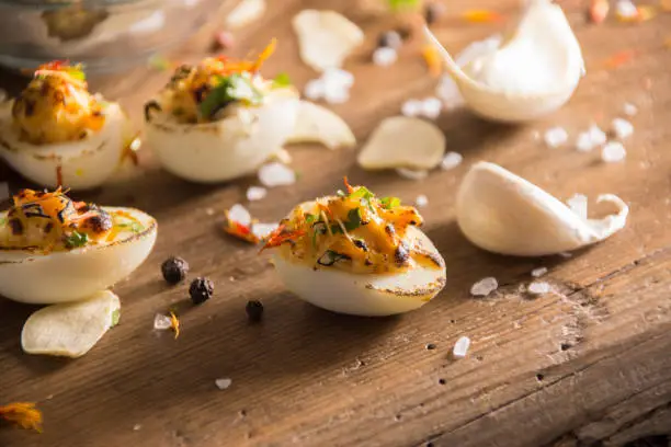 deviled quail eggs arranged and decorated nicely on wooden table. Garlic pods, dried garlic, raw quail eggs in a bowl, parsley sprigs, Pepper corns, Salt crystals arranged around it