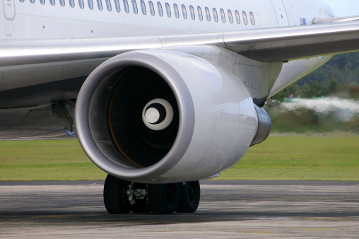 Jet turbine on commercial aircraft emitting exhaust gases while taxiing on ground.