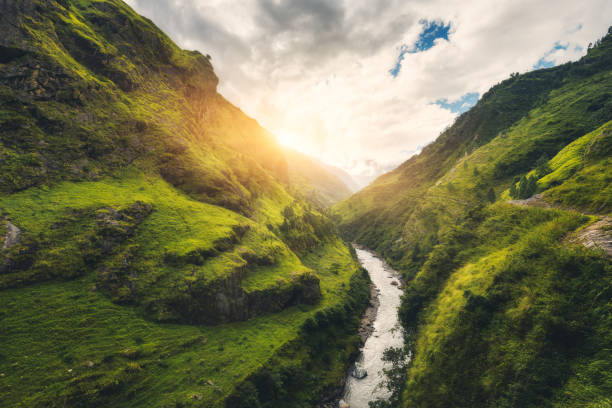 istock View with amazing mountains covered green grass, river, meadows and forest, blue sky with clouds, sun in autumn in Nepal at sunset. Mountain valley at bright sunny evening. Travel in Himalayas. Nature 920377880