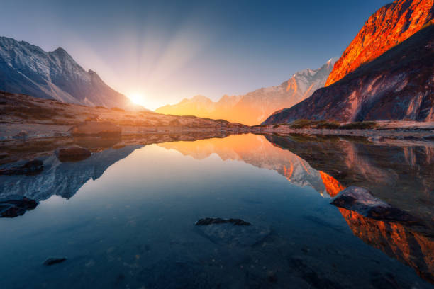 mooi landschap met hoge bergen met verlichte pieken, stenen in bergmeer, reflectie, blauwe hemel en geel zonlicht in sunrise. nepal. geweldige scène met himalaya gebergte. himalaya - zonsopgang stockfoto's en -beelden