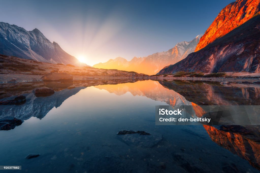 Beautiful landscape with high mountains with illuminated peaks, stones in mountain lake, reflection, blue sky and yellow sunlight in sunrise. Nepal. Amazing scene with Himalayan mountains. Himalayas Landscape - Scenery Stock Photo