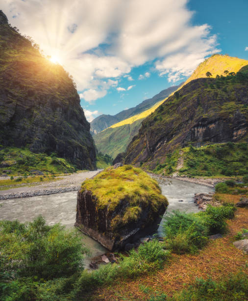 istock Amazing scene with mountains, beautiful river, green forest, blue sky with clouds and big stone in water in autumn in Nepal at sunset. Mountains at bright sunny evening. Travel in Himalayas. Nature 920377892