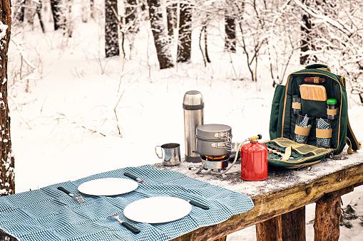 Camping at a table in a winter forest with a backpack, thermos and a burner.