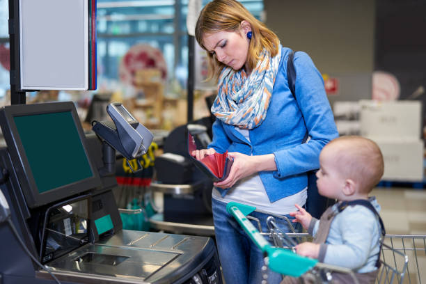 Young woman with baby paying with self checkout Young woman with toddler staying in front of self checkout machine and looking with serious face into her purse self checkout stock pictures, royalty-free photos & images