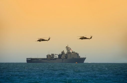 An armed guard looks up at the MV-22 Osprey aircraft while patrolling the deck of USS Tripoli (LHA 7) of the US Navy docked at Garden Island, Sydney Harbour.  This image was taken from Mrs Macquarie's Chair on an afternoon in Spring.