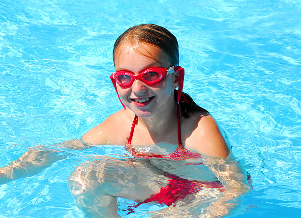 Portrait of a confident teenage girl aged 11 practicing swimming at the swimming pool. The girl is having a break looking out of the pool into the camera.\n