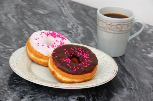 Bright pink sprinkles add a splash of color to glazed donuts and coffee.