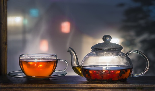 Tea cup with tea pot on the windowsill. Tea on a background of a night landscape. Tea time.
