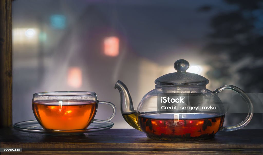 Tea cup with tea pot on the windowsill. Tea on a background of a night landscape. Tea time. Black Tea Stock Photo