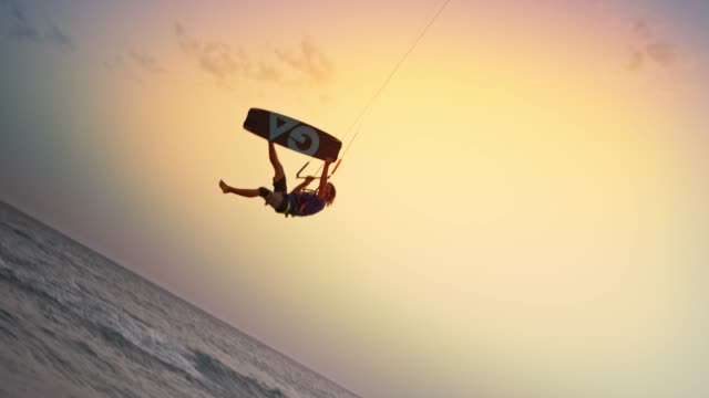 SLO MO Male kiteboarder jumping into the air as the sun is setting