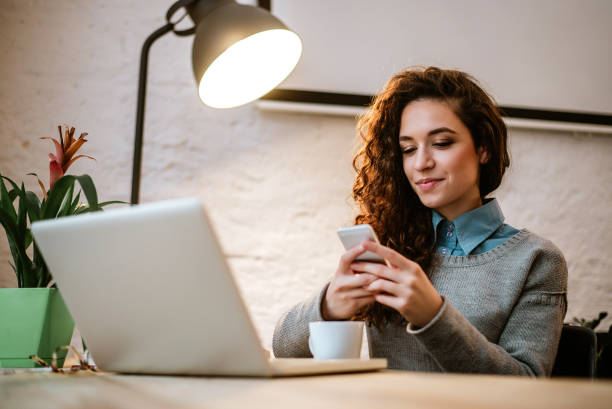 jovem empreendedor no seu local de trabalho usando o laptop e telefone. - computer coffee laptop business - fotografias e filmes do acervo