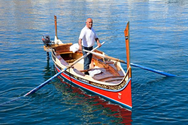 Man steering a traditional Maltese Dghajsa water taxi in the harbour, Vittoriosa, Malta, Europe.