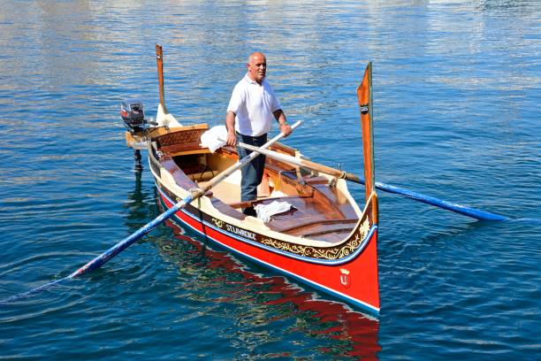 Man steering a Maltese Dghajsa, Malta. Man steering a traditional Maltese Dghajsa water taxi in the harbour, Vittoriosa, Malta, Europe. coconut crab stock pictures, royalty-free photos & images