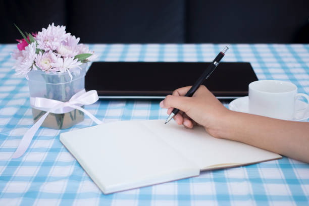 istock female hands with pencil writing on notebook with laptop and flower vase. 920418542