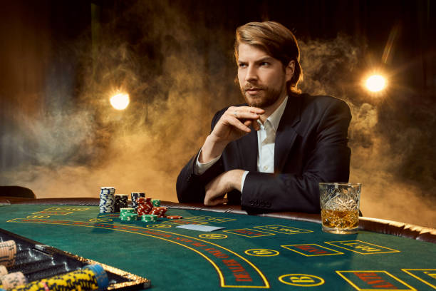 A man in a business suit sitting at the game table. Male player. Passion, cards, chips, alcohol, dice, gambling, casino - it is as male entertainment A man in a business suit sitting at the game table. Male player. Passion, cards, chips, alcohol, dice, gambling, casino - it is as male entertainment. Dangerous fun card game for money. Let the smoke. poker card game stock pictures, royalty-free photos & images