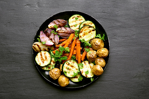 Baked vegetables in plate on black background. Top view, flat lay
