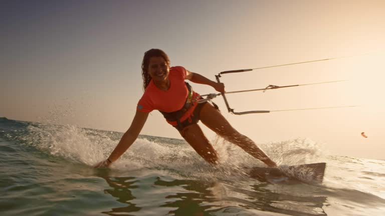 SLO MO Woman riding her kiteboard with one hand in the water and smiling into the camera at sunset