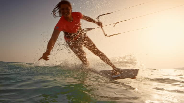 SLO MO Woman kiteboarding at sunset and waving into the camera