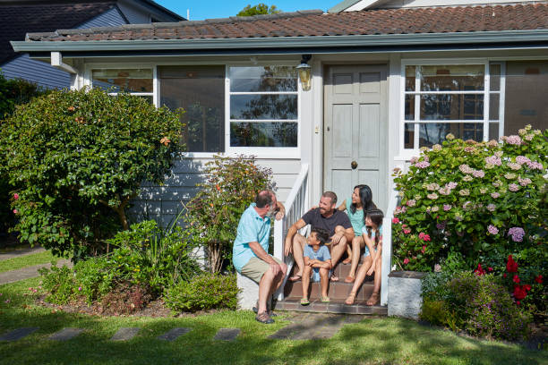 Senior man communicating with family outside house. Multi-generation group is spending time together in lawn. They are wearing casuals on sunny day.