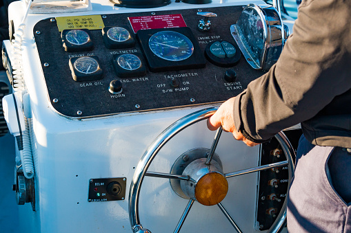 Boat instrument panel, with a Caucasian man with hands on the steering wheel.