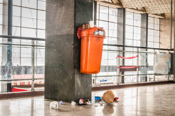 Orange plastic garbage can with overflow junk and litter on the ground polluting indoor space of the building