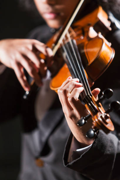 Mixed race teenage boy playing the violin Close-up, cropped view of a mixed race teenage boy, 16 years old, playing the violin, wearing a tuxedo. The focus is on his hand.  He is African-American, Asian and Hispanic. solo performance stock pictures, royalty-free photos & images