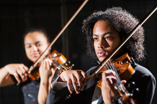 Teenagers playing violins in concert, focus on boy Two mixed race teenagers performing together in a concert, playing violins on stage. The 15 year old girl is Hispanic, black and Caucasian. The focus is on the boy, 16, who is Hispanic, Asian and African-American. violinist photos stock pictures, royalty-free photos & images