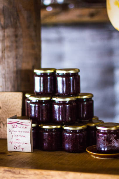 Fresh plums and jar of plum jam on wooden table in kitchen, teaspoon in jar.