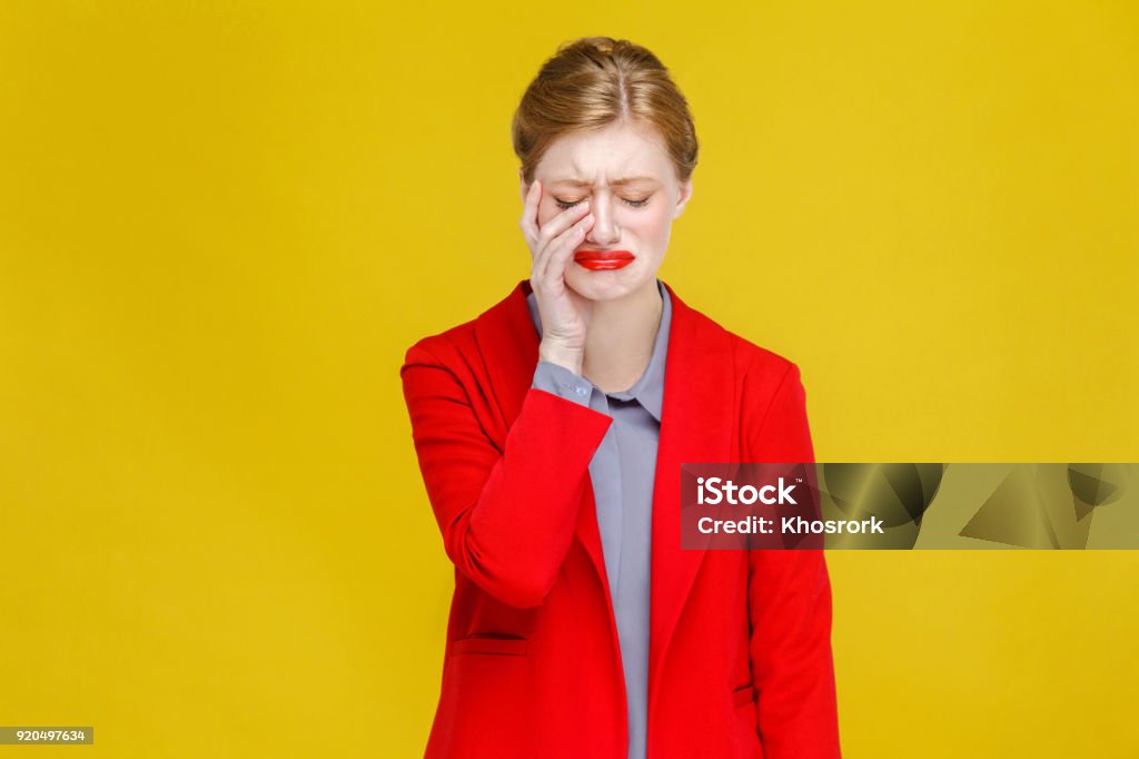 Ginger red head business woman in red suit have tooth pain. Ginger red head business woman in red suit have tooth pain. Studio shot, isolated on yellow background Crying Stock Photo