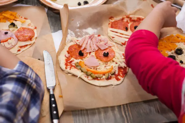 Photo of Master class for children on baking funny halloween pizza. Young children learn to cook a funny monster pizza. Kids preparing homemade piizza. Little cook.