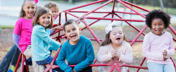 Children playing on playground monkey bars A group of preschool and elementary school children, 5 to 7 years old, on the playground, climbing on monkey bars. The girl with the white bow in her hair has down syndrome. jungle gym stock pictures, royalty-free photos & images