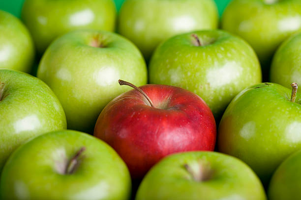 A red apple in a collection of green apples stock photo