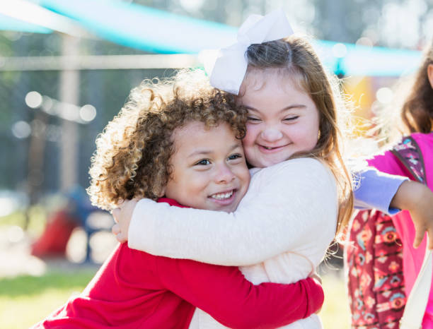Little girl with down syndrome and boy hugging A pretty little girl with down syndrome and her cute 5 year old friend with curly hair, hugging each other and smiling.  The boy is mixed race African-American and Caucasian. down syndrome stock pictures, royalty-free photos & images