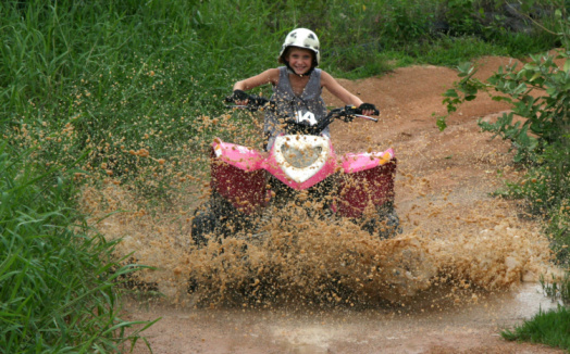 Excited attractive young girl rides a Quad Bike through mud after heavy rains in Thailand. Girl is smiling with delight as water and mud spray over her and the bike.