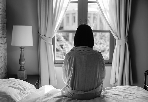 Lone woman sitting on the bed looking out at the window in the morning in black and white